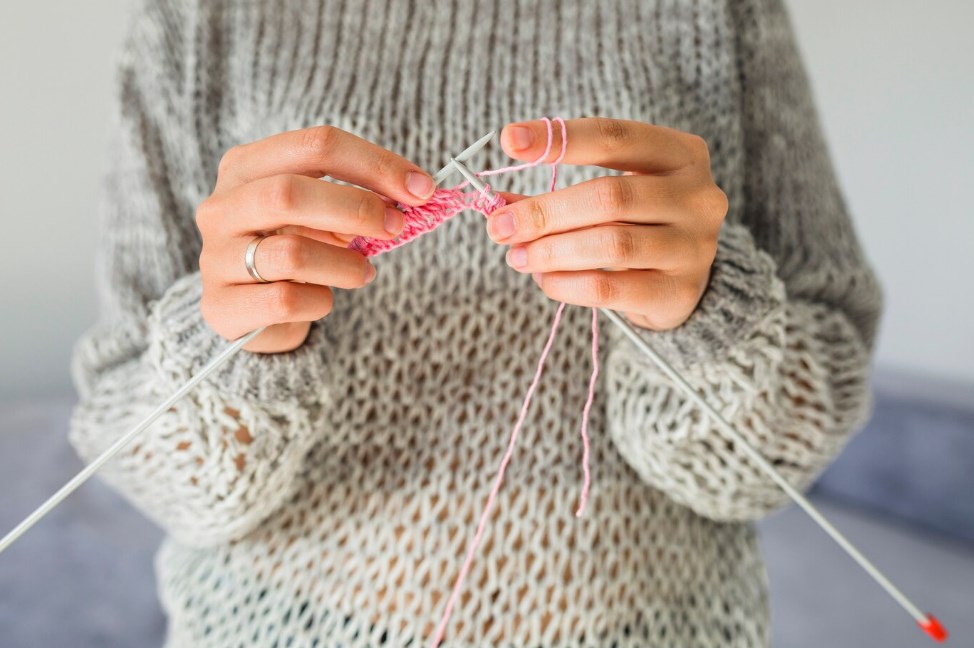 a woman in a grey sweater knitting with a crochet
