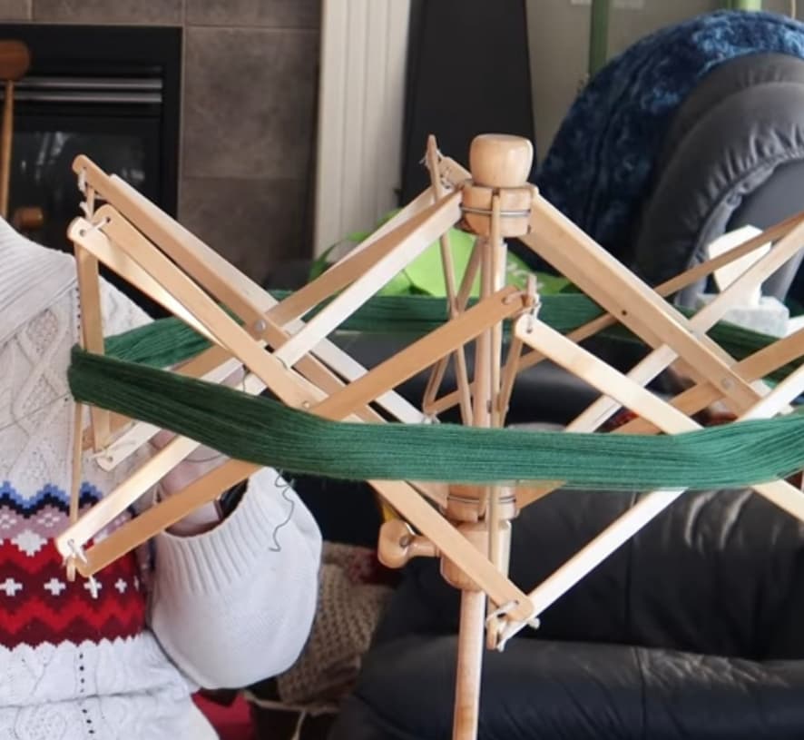 A wooden yarn swift with green yarn wound around it, set up in a living room