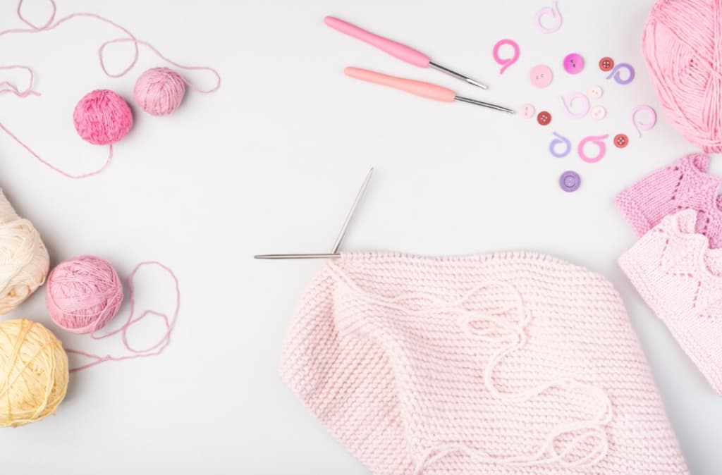 A neat knitting setup with pink yarns and needles on a white background