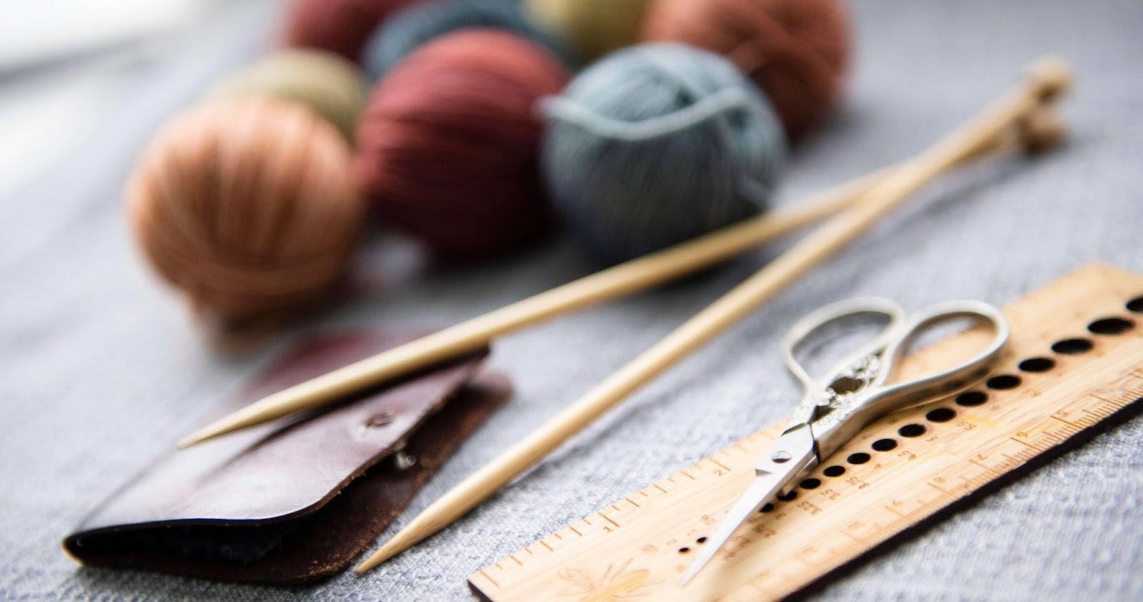 Scissors, ruler, thread and knitting needles for sewing on the table