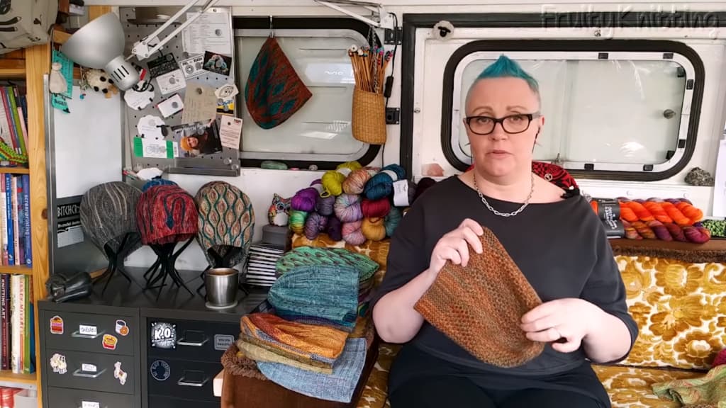 A woman holding a piece of knitting, an array of knitted hats displayed on the shelf