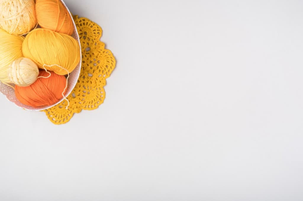 Yellow yarn balls on crochet doily with room for text on white table