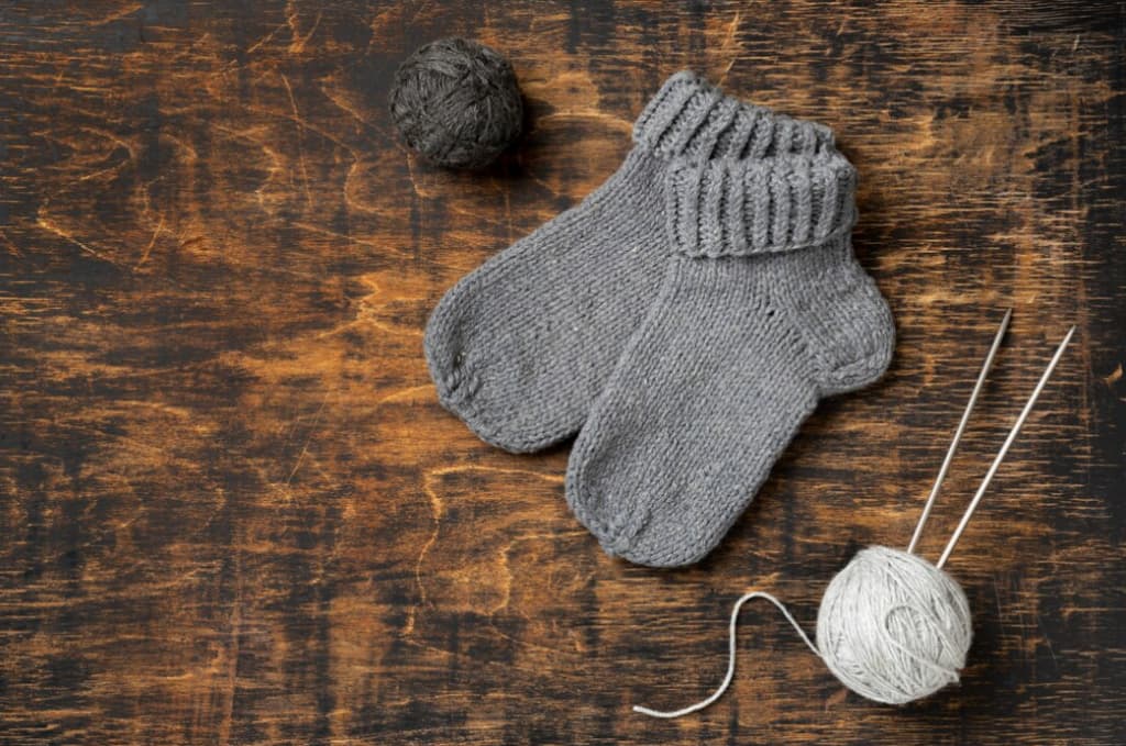 Hand-knitted gray socks and yarn balls on a wooden surface