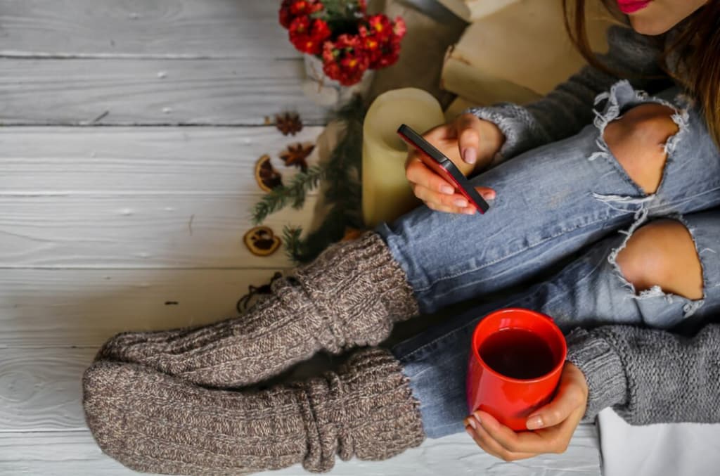 Overhead view of a person with cozy socks holding a red mug and phone