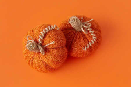 Two orange knitted pumpkins with vines and leaves on an orange backdrop