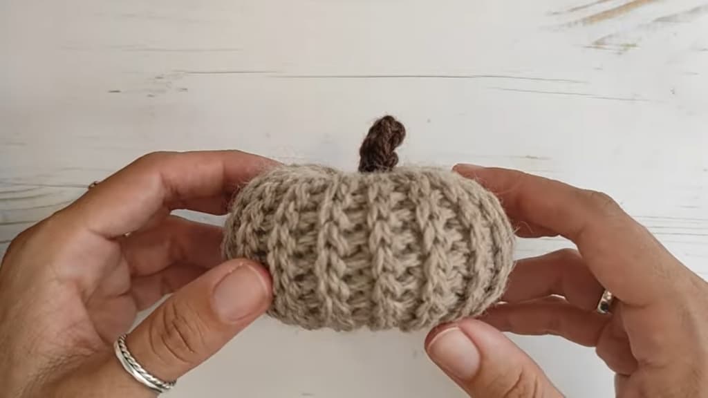 Hands holding a knitted pumpkin with a curled stem on a white background