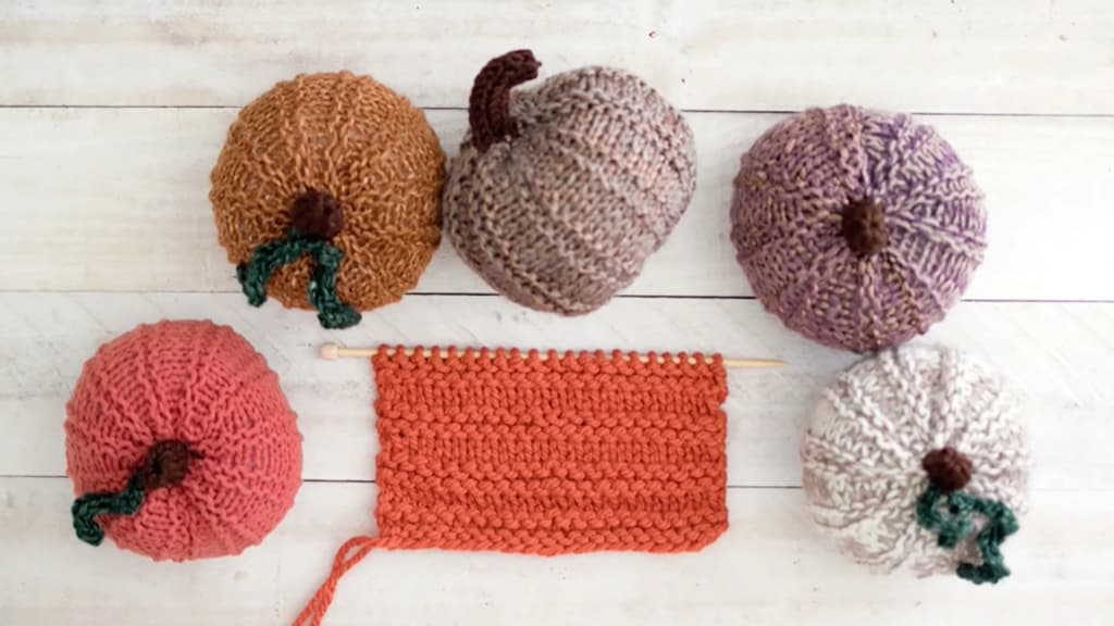 A collection of five knitted pumpkins in assorted colors on a wooden surface