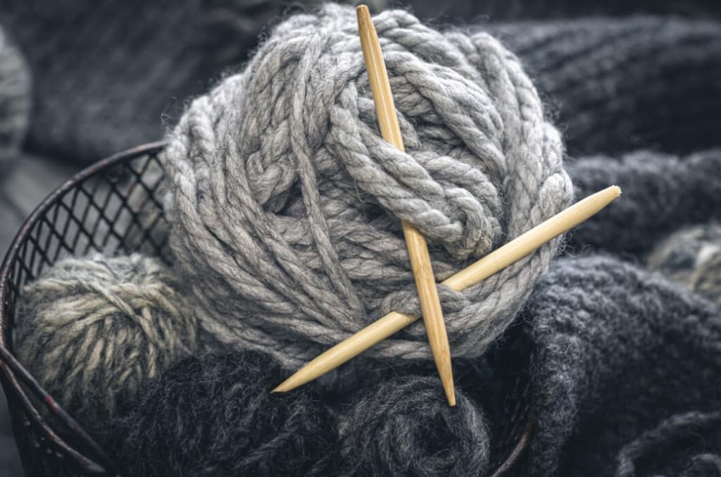 A basket with grey yarn and knitting needles