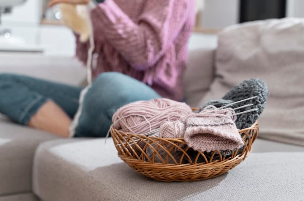 Basket with yarn and knitting needles beside a person on a couch
