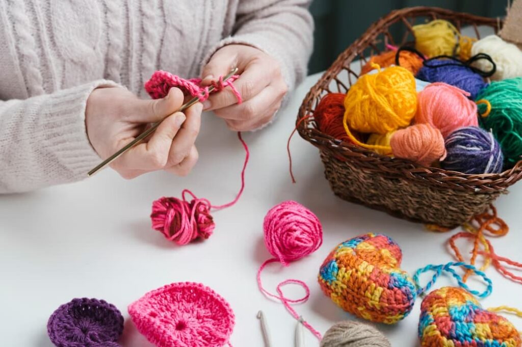 Close-up of hands knitting with pink yarn and a basket with colorful threads