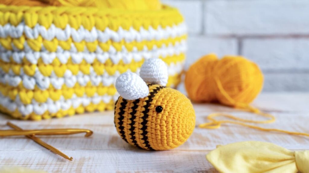 Handmade yellow and black crocheted bee with white wings, the knitted yellow basket behind